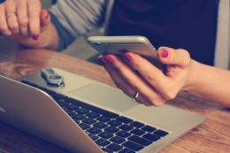 image of person behind a laptop with smartphone in her hands